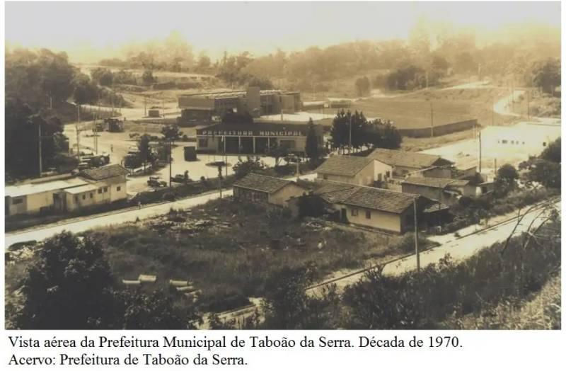 Vista aérea da Prefeitura Municipal de Taboão da Serra, anos 1970, com ruas, casas e vegetação ao redor; clima rural e antigo.