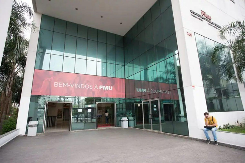 Entrada de prédio moderno de vidro da FMU, com faixa Bem-vindos à FMU e um estudante sentado na lateral.