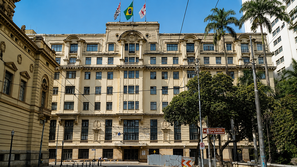 Prédio histórico bege no centro, com bandeiras do Brasil e de SP, palmeiras e placa Galeria Olido, na Praça da República.