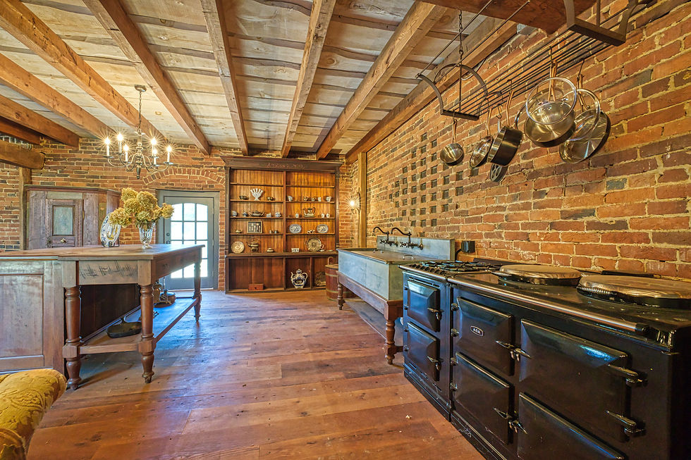 The kitchen in the restored 1813 barn — original brick walls with the historic diamond-pattern ventilation openings still intact, hand-hewn timber beams, wide-plank hardwood floors, and an AGA range.