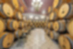 Rows of oak wine barrels aging in the Pearmund Cellars barrel room, set with small tasting tables and gold chairs