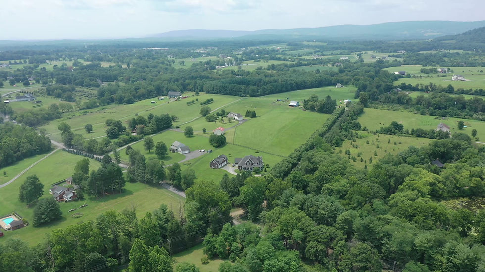Aerial view of a western Loudoun County property surrounded by pasture and hayfields with the Blue Ridge Mountains on the horizon