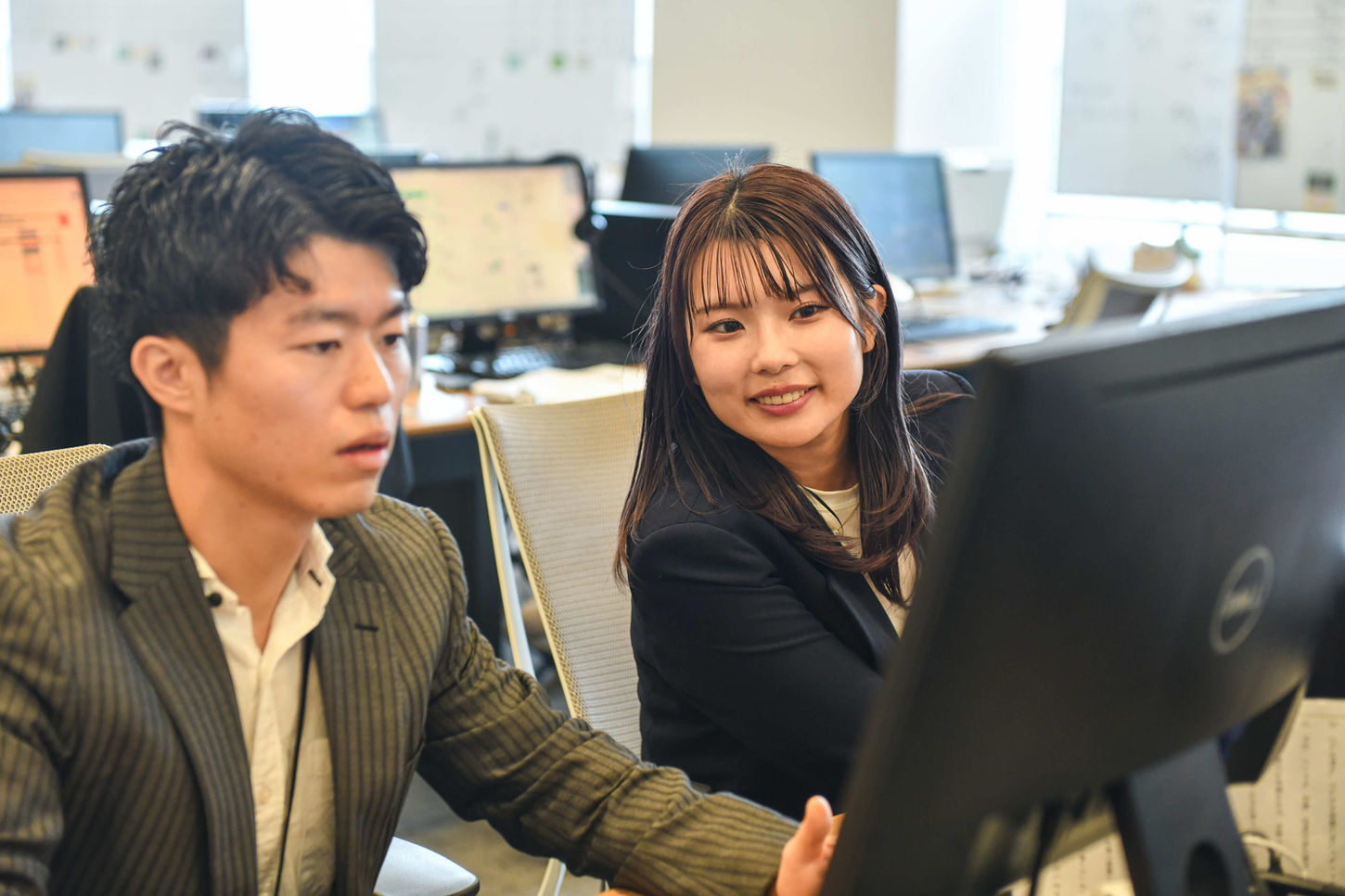 オフィスでPC画面を見ながら打ち合わせをする男女の社員