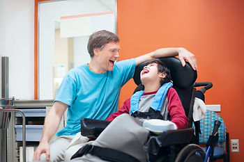 A father is laughing with his disabled young son in a wheelchair.