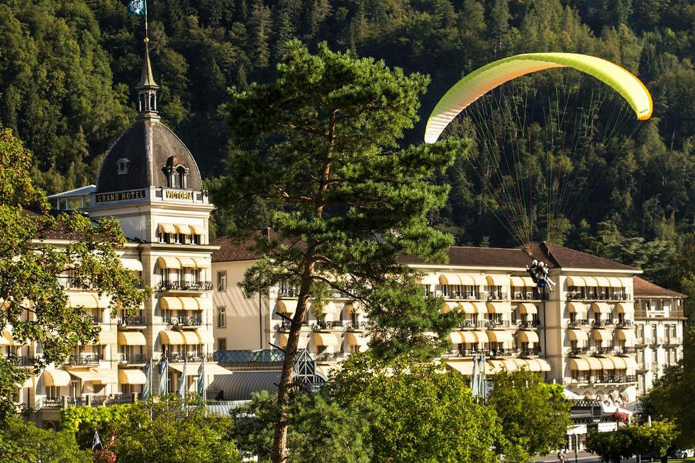 Paraglider soaring over a grand hotel in Switzerland.
