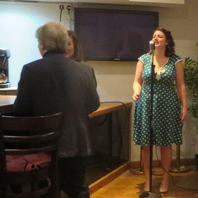 Person singing into a microphone in a green polka-dot dress