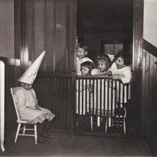 Children looking at a child on a stool wearing a paper hat
