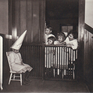 Children looking at a child on a stool wearing a paper hat