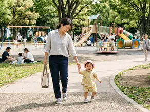 ママと１歳の子が手をつないで公園を歩いている