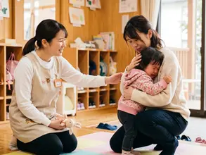 保育園で泣く子どもと見守る親と保育士