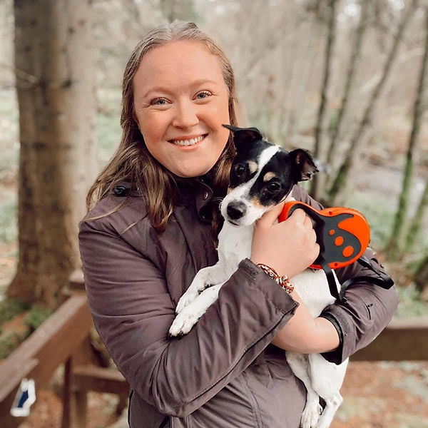 blonde girl in brown jacket holding a tri colour jack russell and red/black flexi lead
