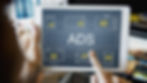 Tablet displaying "ADS" with icons of TV, news, and email ads. A hand points at the screen. Background shows blurred office setting.