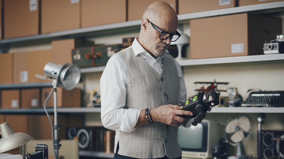 Man examining a vintage camera in an antique appraisal studio filled with retro items and old electronics.