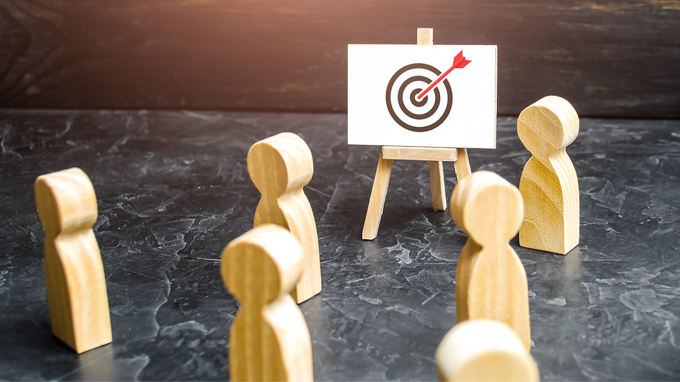 Wooden figures face a small easel with a target and red arrow on a dark surface, suggesting focus and goal-setting.
