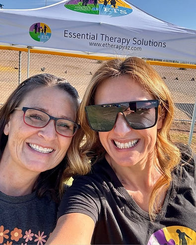 Two smiling Essential Therapy Solutions team members at a recruitment event under a branded canopy tent