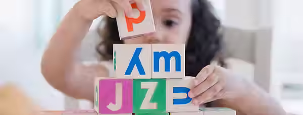 Child stacking colorful alphabet blocks during a pediatric therapy session