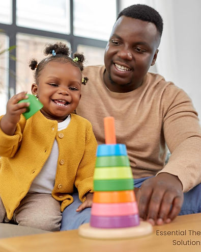 Smiling child stacking colorful rings with a supportive adult during a therapy session