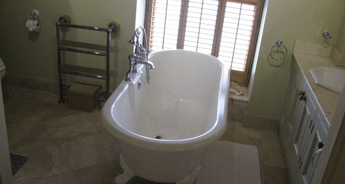 Clean bathroom with freestanding bathtub, shuttered window, towel rail and vanity unit.