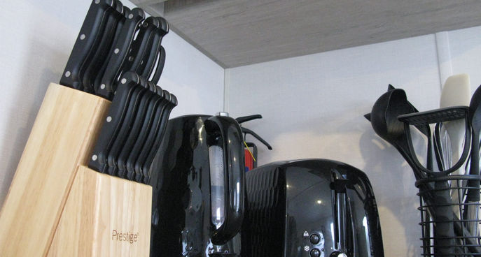 Clean kitchen countertop with knife block, kettle, toaster and utensils neatly arranged.