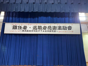舞台上、紺色の幕の前にある「離任者・退職者感謝激励会」と書かれた横断幕。