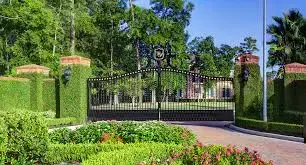 Elegant iron gate entrance to a large home with lush landscaping private security company Houston