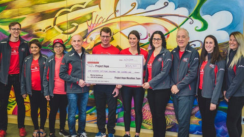 Ten people wearing red shirts hold a large check addressed to Project HOPE.