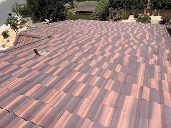A view of a Riverside residential roof with reddish-brown curved tiles, a vent pipe, and landscaping visible in the background—perfect for showcasing professional roof cleaning or soft wash results.