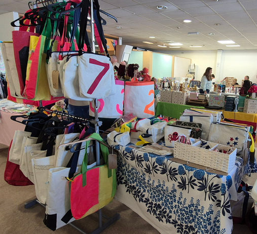 Busy Indoor Market with different stalls. In front different coloured Sail Bags