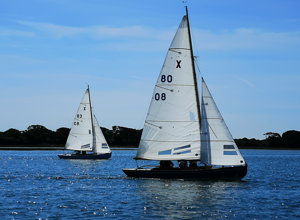 two sail boats on the water, both have 2 sails up. Sky and water are dark blue
