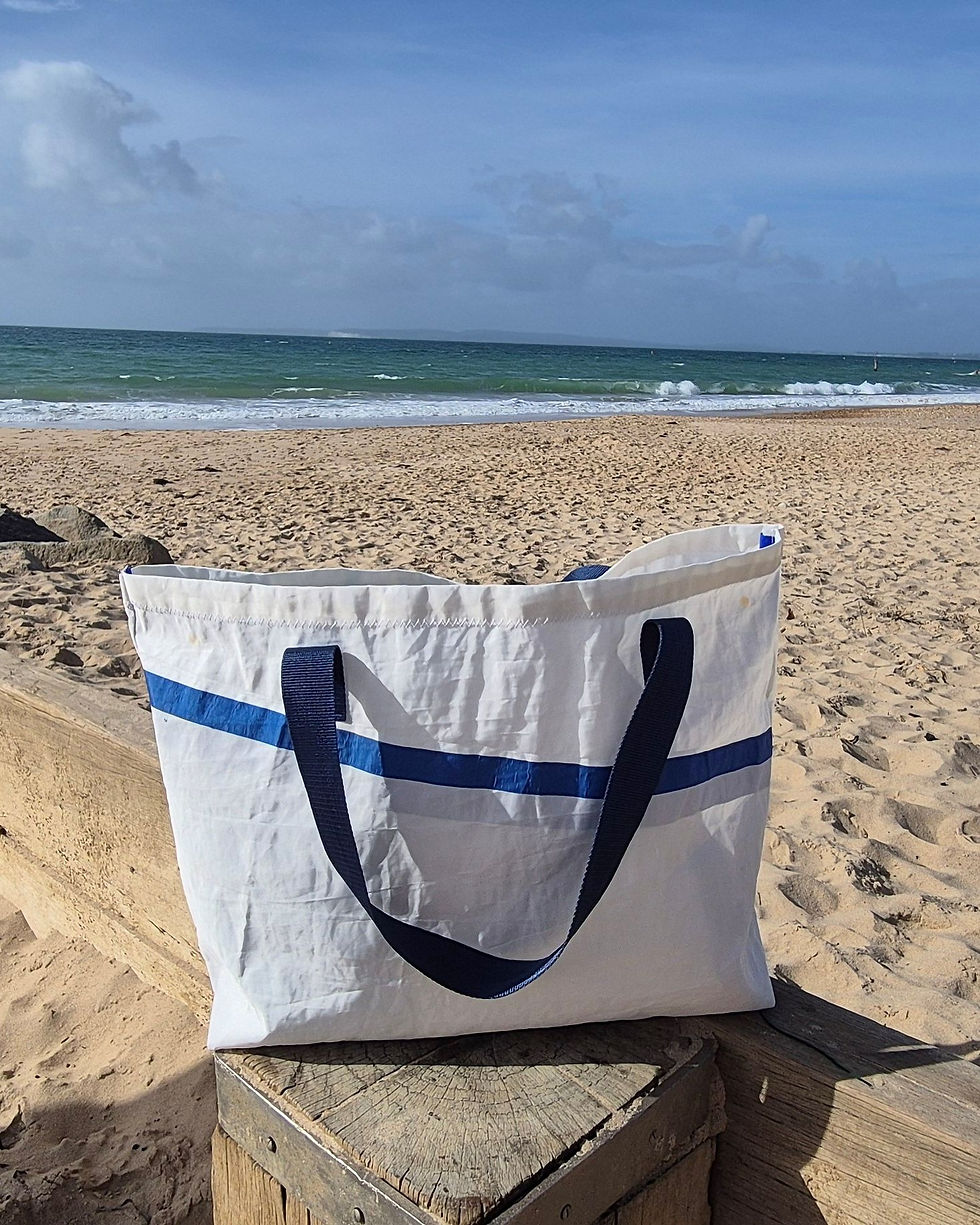 White Sail Bag with blue stripe left to right and blue handles on the beach