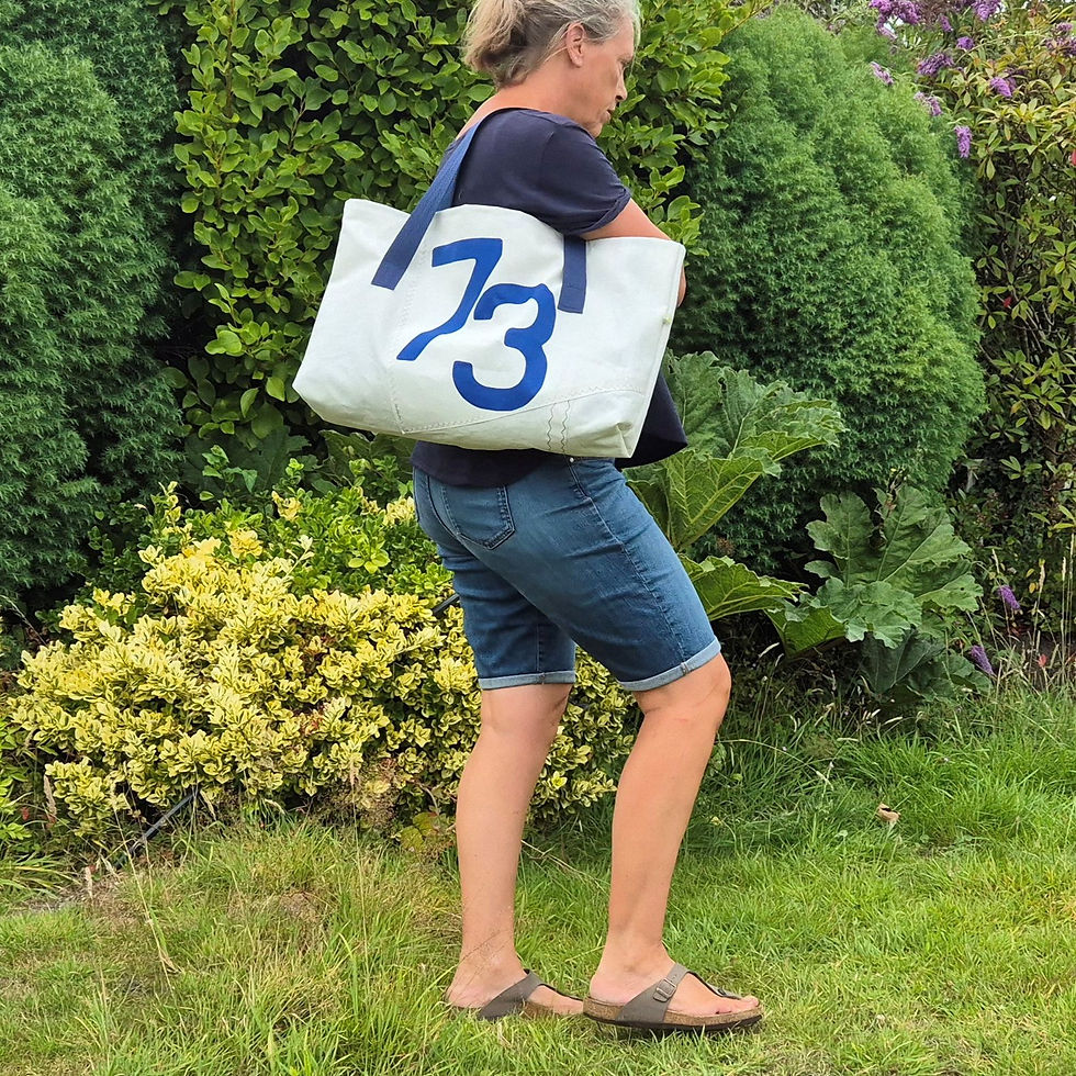 Thumbnail: person carrying white sail bag with blue nautical no. 73 and blue handles over the shoulder, in garden setting