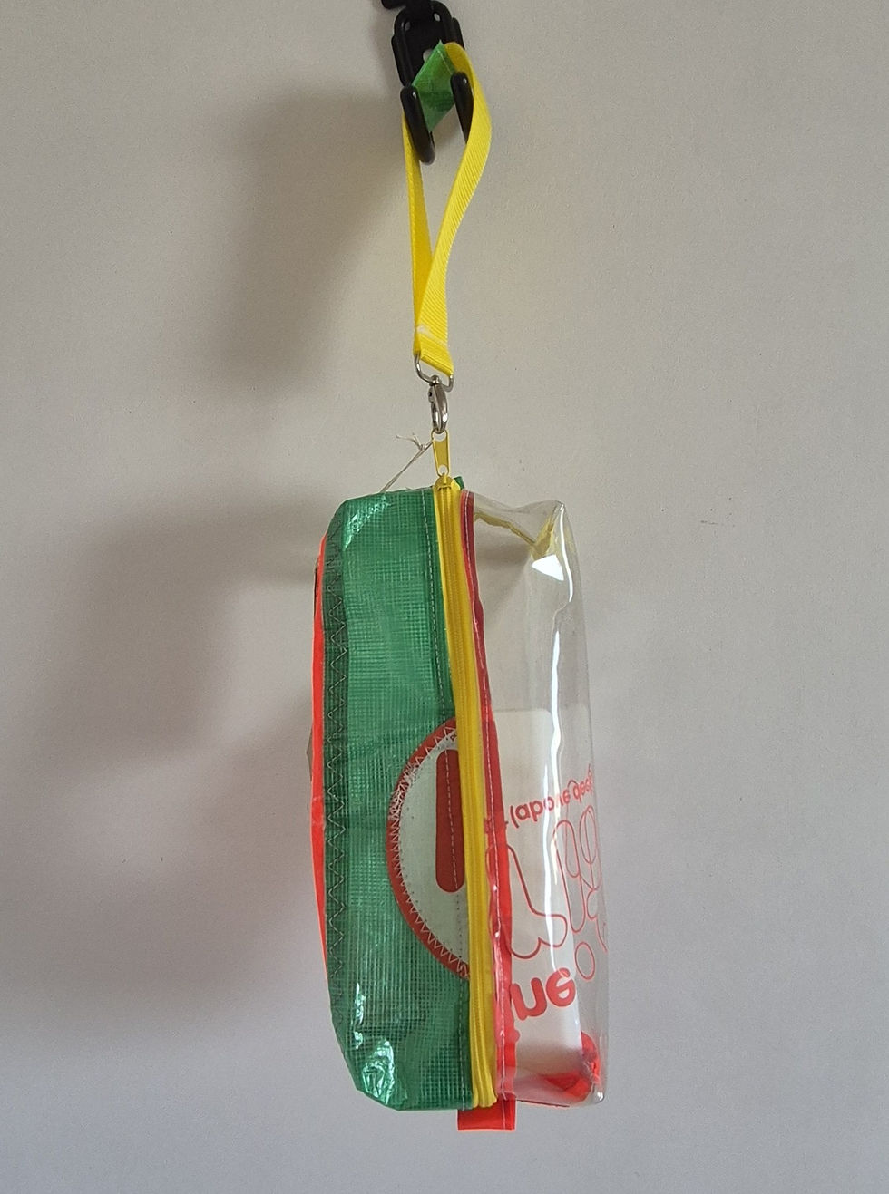 Thumbnail: A clear pencil case with a red, green, and yellow fabric top. The case has a yellow zip and a yellow fabric handle. The case