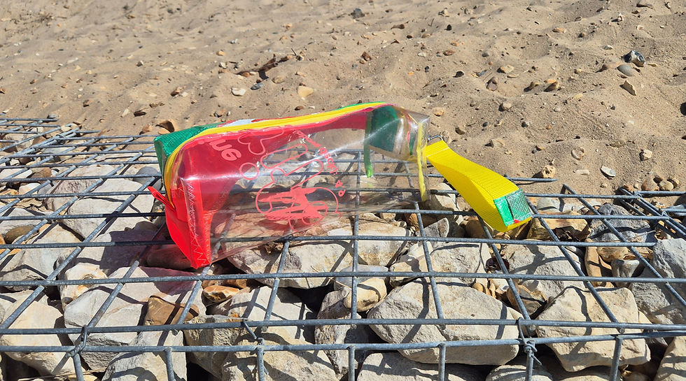 A clear pencil case with a red, green, and yellow fabric top. The case has a yellow zip and a yellow fabric handle.