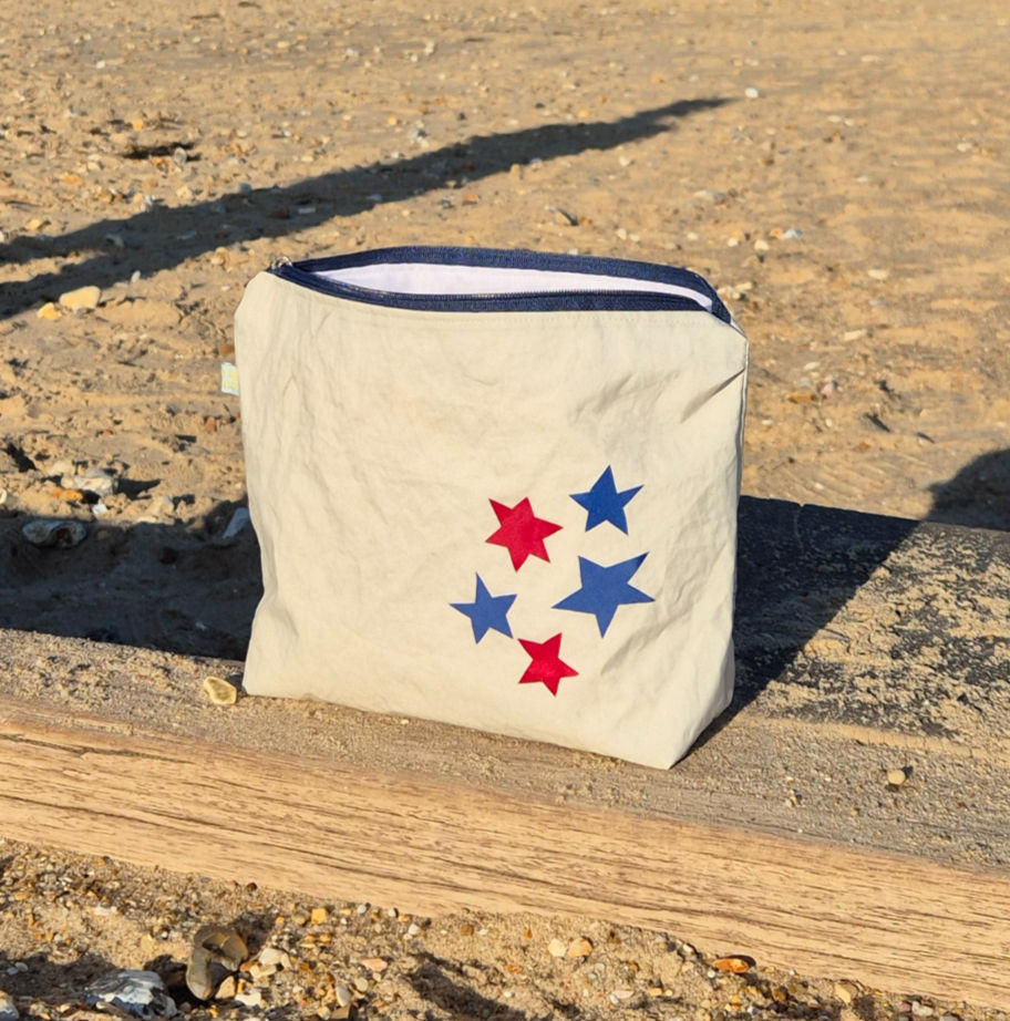 off-white Sailcloth pouch with red and blue stars on the left and blue zip on top. in a beach setting