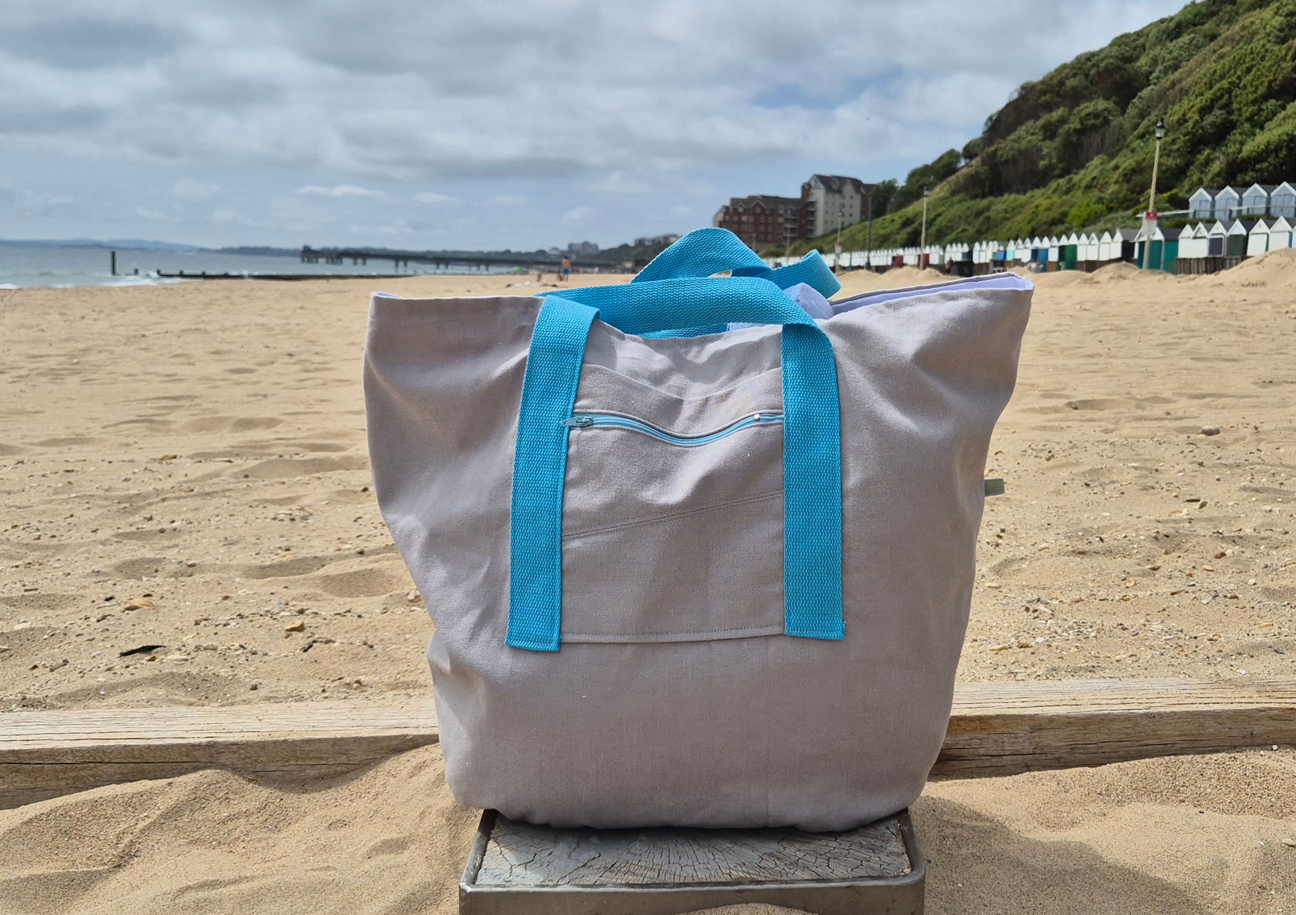 Grey Cotton Bag with light blue Handles and light blue front zip. Beach setting