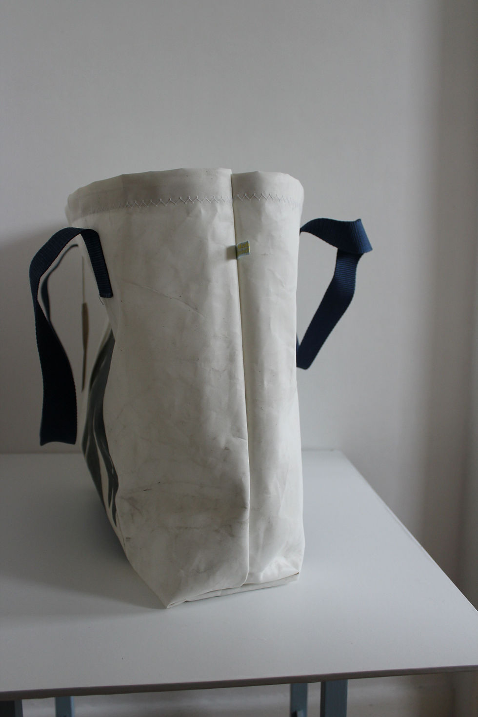 Thumbnail: Side view of the white sail bag with blue handles. seams are meeting on white background.