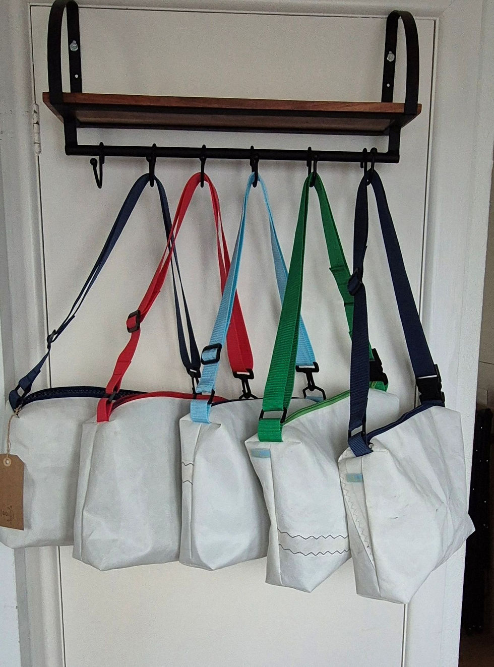 5 white Sail bags hanging on wardrobe with black hooks and white background. the handles are all different. From left to righ