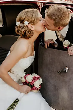 Brautpaar bei einem spontanen Kuss am Hochzeitsauto
