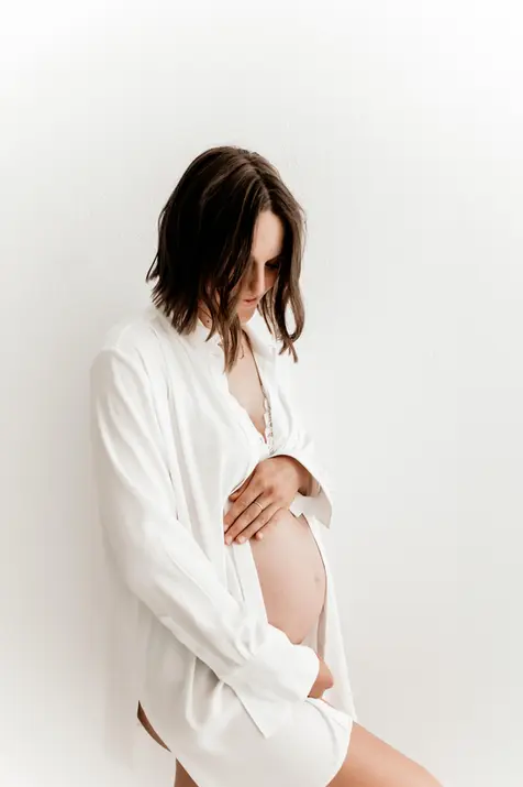 Seitliche Aufnahme einer werdenden Mama im weißen Hemd mit sichtbarem Babybauch