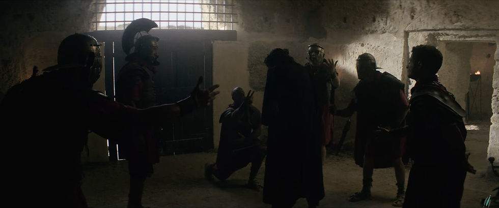 Roman soldiers kneel and bow in mockery in a stone guardroom