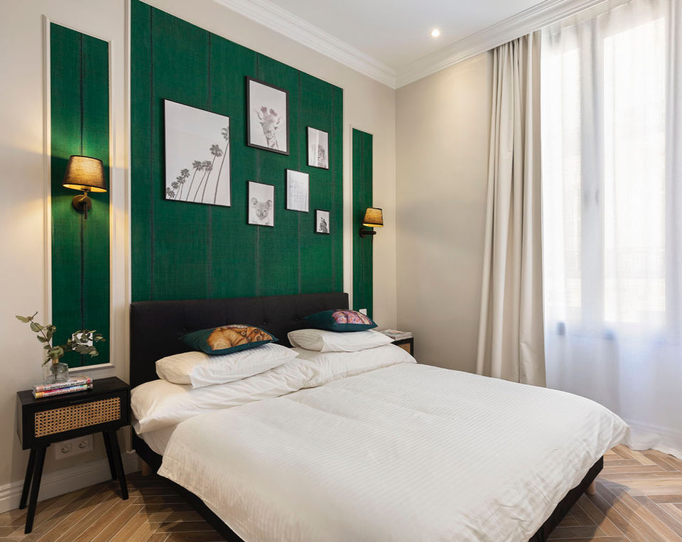 Chambre moderne et élégante avec mur vert texturé derrière la tête de lit, lit double avec linge blanc, tables de chevet noires, appliques murales et grandes fenêtres avec rideaux blancs.