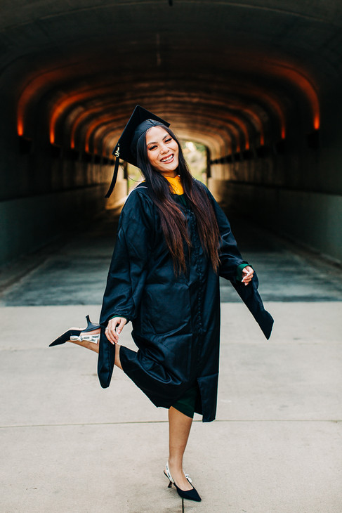 women dressed in graduation cap and gown laughing and kicking her foot out