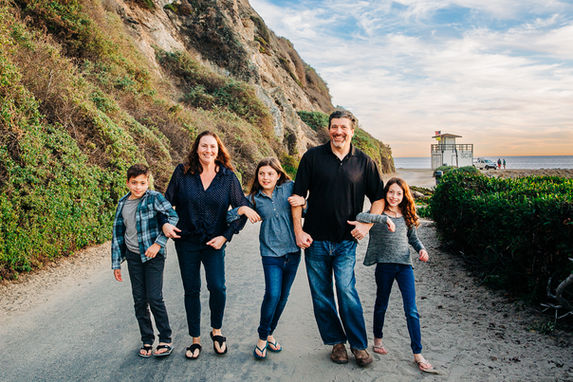 family walking with linked arms with cliffs and the beach behind them