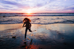 A girl running way from the ocean waves at sunset