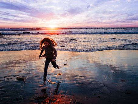 A girl running way from the ocean waves at sunset