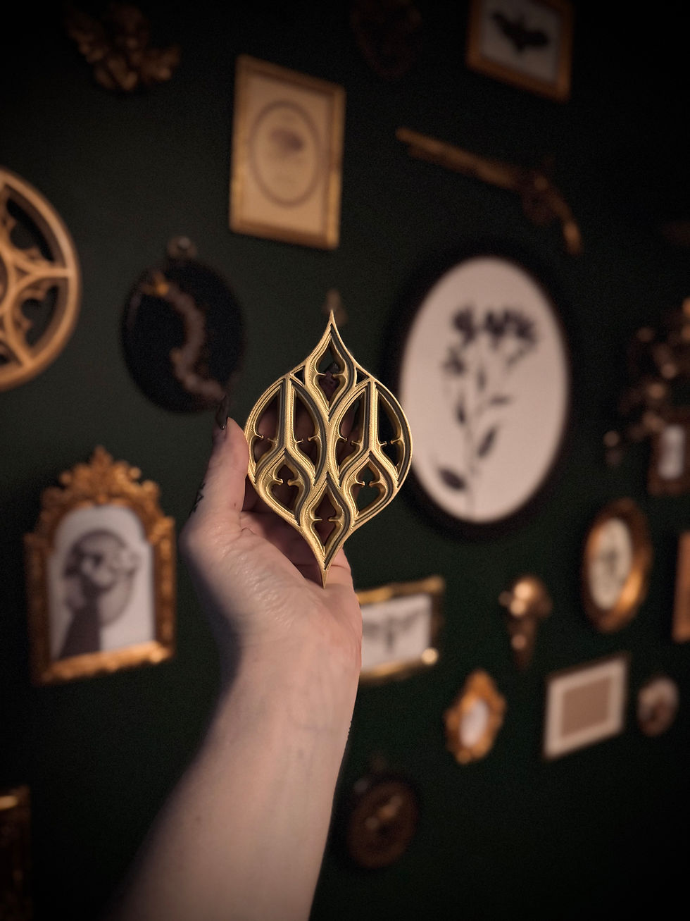 Thumbnail: Hand holding gold gothic lancet wall piece against dark green gallery wall