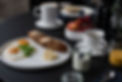 Detailreiche Food-Fotografie – Frühstücksplatte mit Spiegeleiern, Laugenstange, Jogurt und Cappuccino im Morgenlicht Tisch mit schwarzem Linoleum