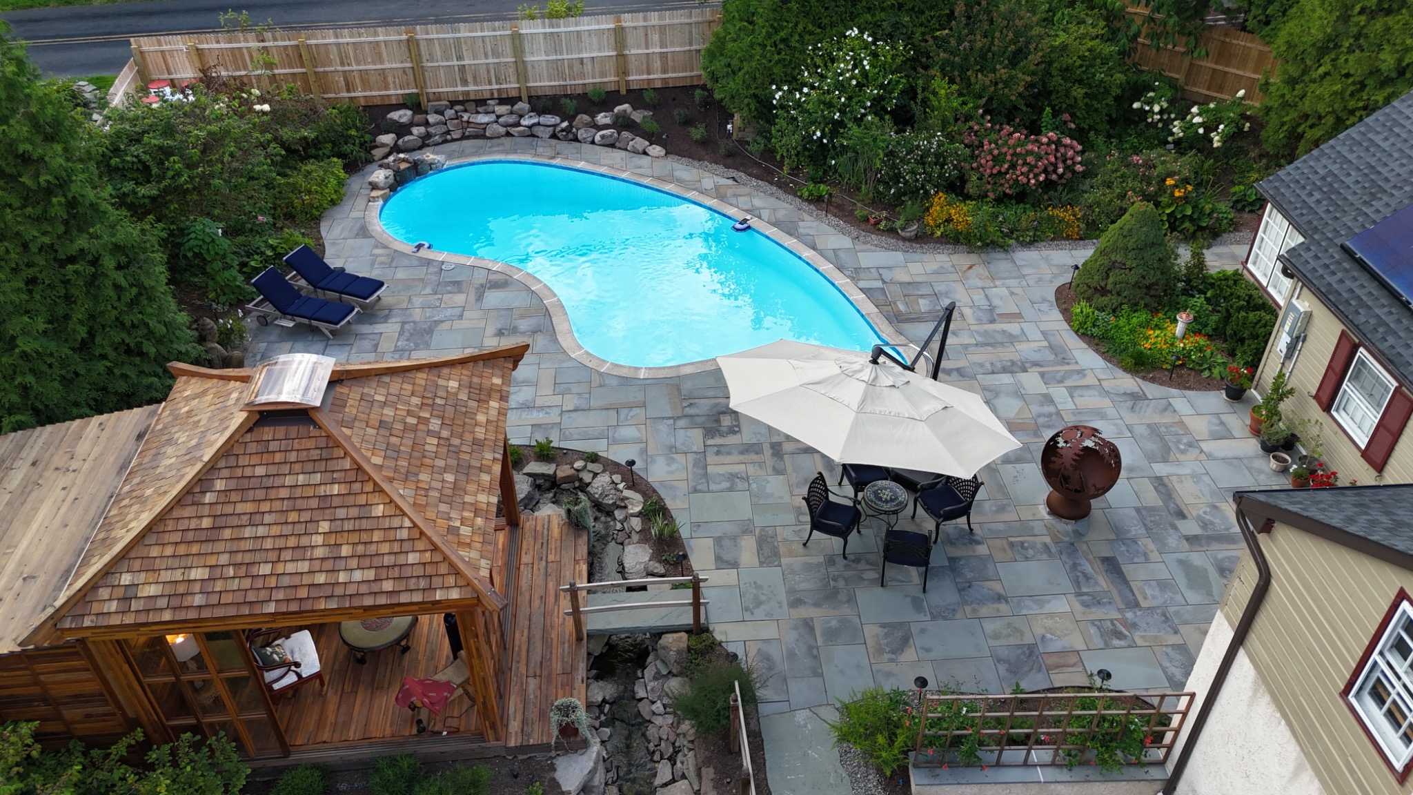 Original ArdeaDrones daytime drone photograph of an outdoor swimming pool, stone patio and wood pavilion