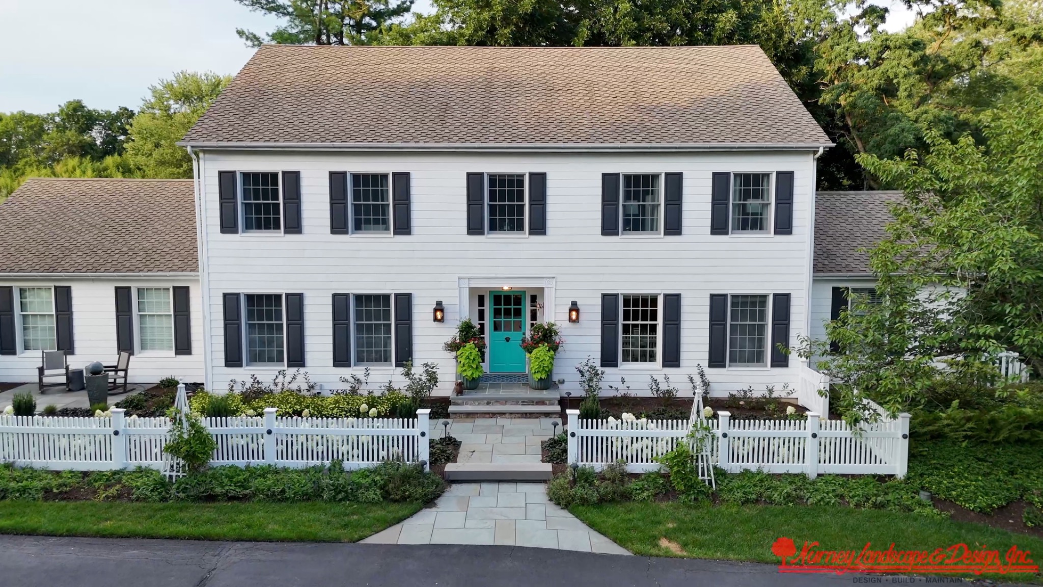 Original daytime photograph of white colonial residence with teal entry door and picket fence, with Nurney Landscape branding
