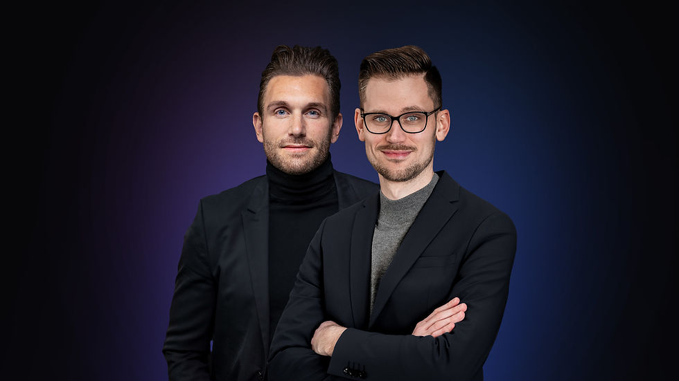 Zwei junge Männer lächeln selbstbewusst in Anzügen vor dunklem Hintergrund.